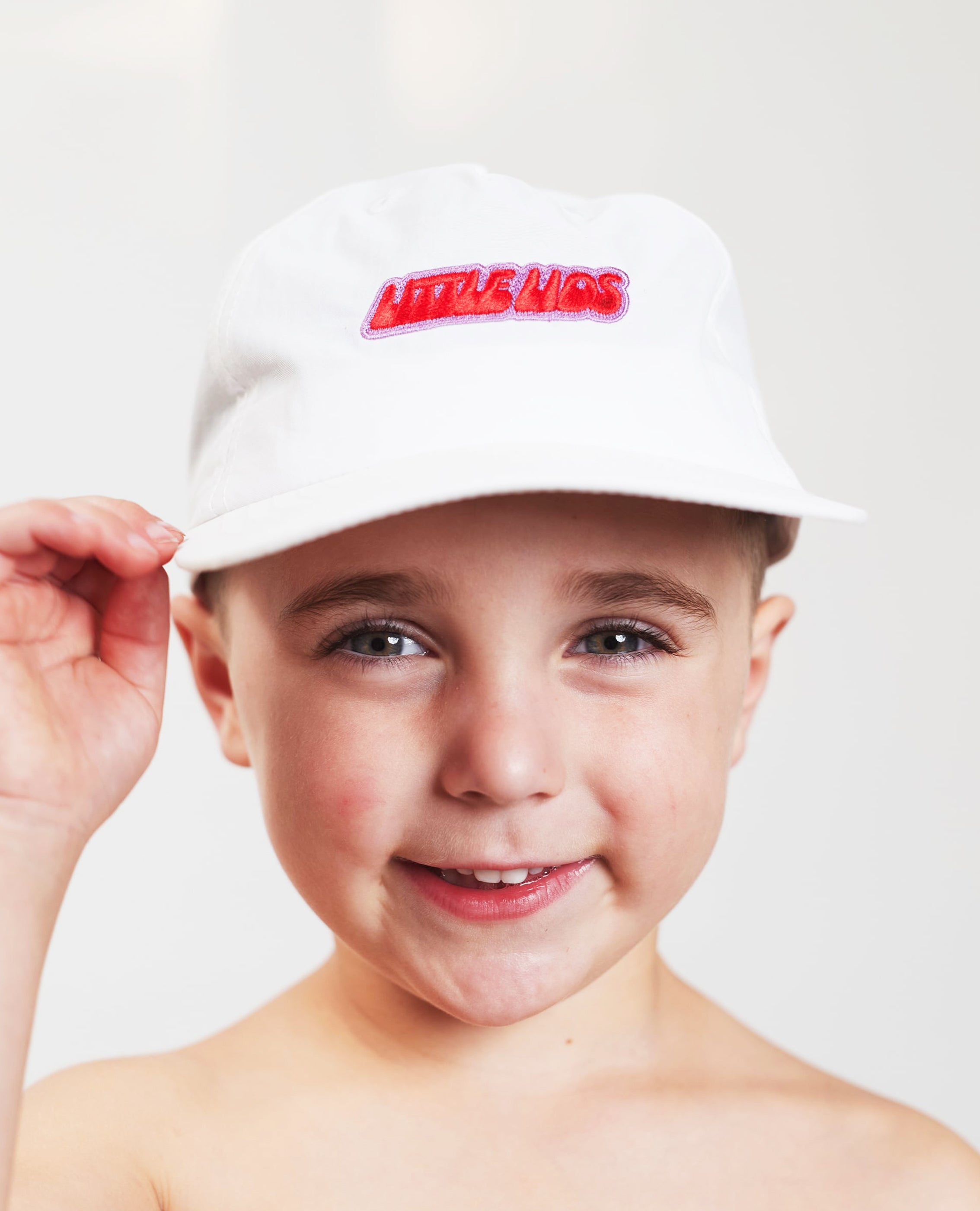 Kid wearing a white kids hat with 'LITTLE LIDS' Red and pink logo